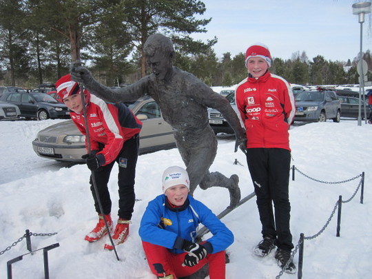 Hans Ole Røen Halle (t.v), Kristoffer sittende og Erlend Jonli ved skistatuen av Oddvar Brå